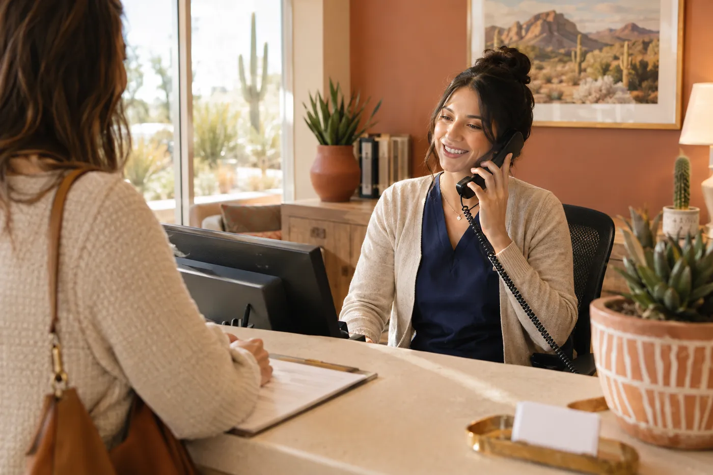 Clinic staff member answering a desk phone while a patient checks in